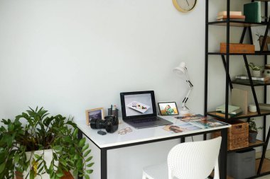Dizüstü bilgisayar, dijital kamera ve fotoğrafçı masasında basılı fotoğraflar.