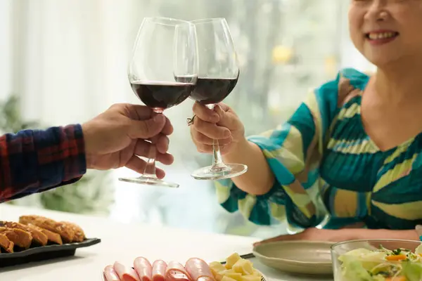Happy elderly couple toasting with wine glasses when having romantic dinner at home
