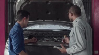 Araba servisindeki motor ve motor çalışmalarını incelerken araba kaputuna bakan tamirci ve erkek istemcinin arka görünümü