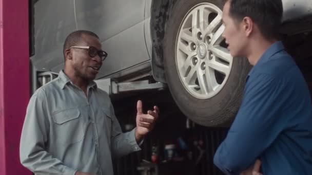 中长的非洲裔美国轮胎适配者在汽车维修站向人们解释轮胎修理的原因 — 图库视频影像