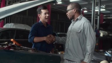 Asyalı bir adamın Afrikalı Amerikalı bir uzmanın el sıkışırken orta boy fotoğrafı. Servis merkezinde araba tamirinden bahsediyor.