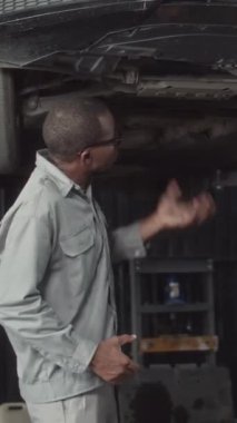 Teknisyenin arabanın altında duran yağ sızıntısını açıklayan dikey görüntüsü.