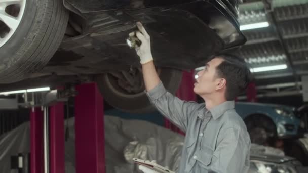 Handhållen Bild Asiatisk Mekaniker Grå Uniform Inspektera Bil Botten Med — Stockvideo