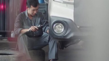 Servis istasyonundaki müşteriler için Asyalı tamircinin araba tekerleğini değiştirdiği orta boy bir çekim.