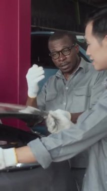 Benzin istasyonunda araba kaputunu inceleyen çoklu etnik mekaniklerin dikey çekimi