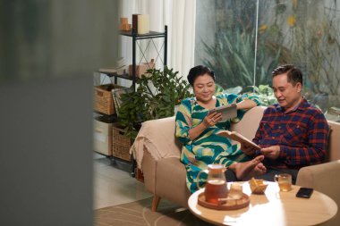 Yaşlı Vietnamlı çift akşamlarını evde geçirip dijital tablette kitap okuyup, televizyon seyrediyor.