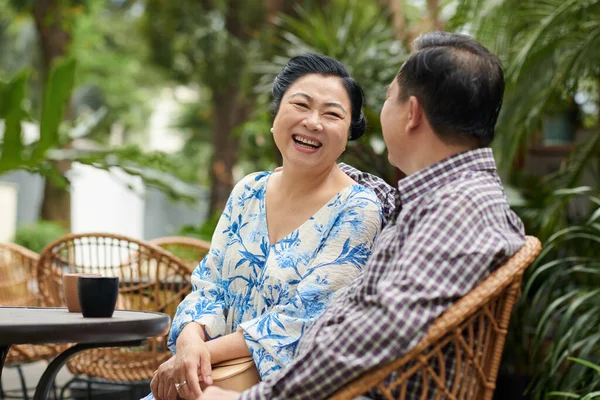 Senior woman laughing at joke of her boyfriend when they are sitting at table in outdoor cafe
