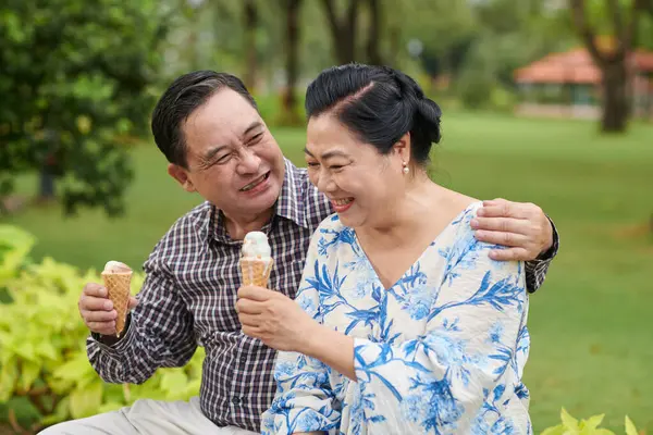 Cheerful senior couple eating ice-cream when enjoying romantic date in park