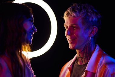 Boynunda dövmesi olan gülümseyen genç bir adam gece partisinde ya da çılgın bir kızla konuşuyor.