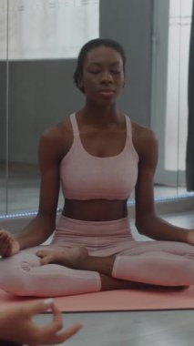Stüdyoda yoga yaparken Lotus pozisyonunda meditasyon yapan siyah bayan sporcunun dikey çekimi.