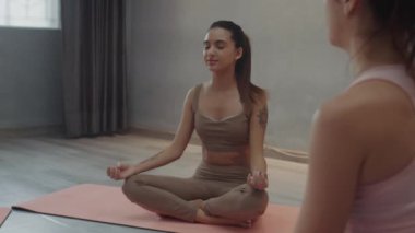 Hocayla yoga yaparken Lotus pozisyonunda gözleri kapalı oturan rahat bir kadının orta uzunlukta bir pozu.