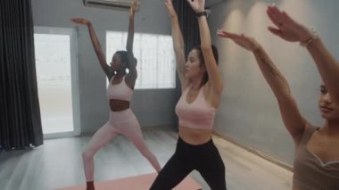 Yoga dersinde kadın sporcuların kol ve vücut esneme egzersizleri yaptığı orta boy bir çekim.