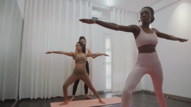Spor eğitmeninin spor salonlarında spor yaparken yoga asanalı kadınlara yardım edişini çek.