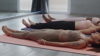 Konforlu modern stüdyoda yoga yaparken çeşitli spor kadınlarının yerde ceset pozu çalışmalarını çekiyoruz.