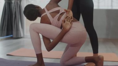 Kadın çalıştırıcının yardımıyla arkadan kollarını kavuşturup yoga yapan kadının arkadan görünüşü.