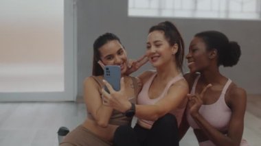 Gülümseyen çok kültürlü kızların fitness dersinin başlamasını beklerken akıllı telefondan selfie çekerkenki görüntüsü.