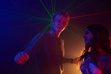 Gençler çılgın bir partide neon ışıkta dans ediyorlar.