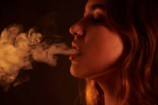 Young woman with piercing exhaling smoke of hookah