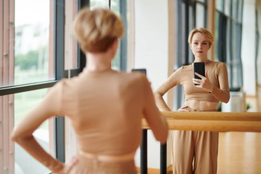 Fit kadın dansçı uzun kollu üst ve geniş pantolon stüdyo aynasında selfie çekiyor.