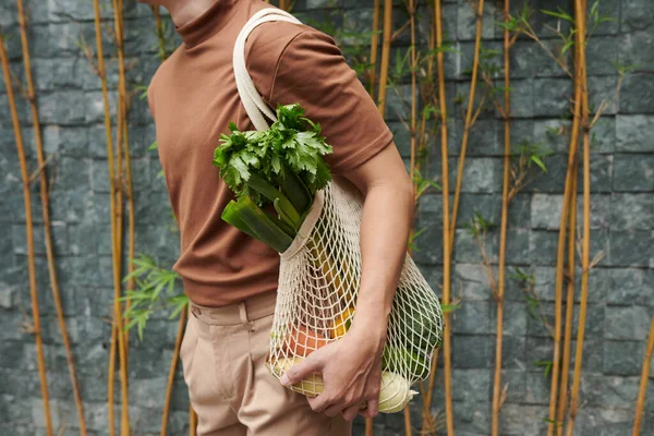 地元の市場で買った新鮮な食料品のメッシュバッグを持っている若者 — ストック写真