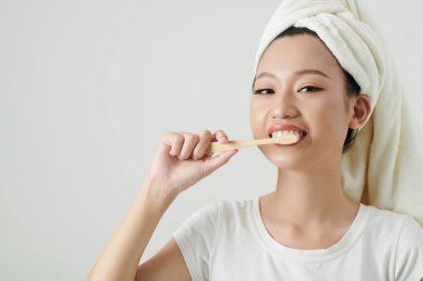 Kafasında havluyla dişlerini fırçalayan neşeli Vietnamlı bir kadının portresi.