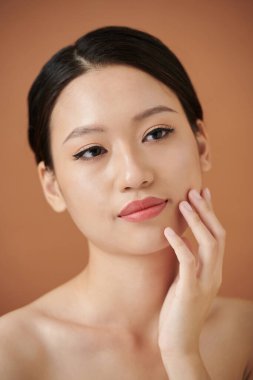 Spa işleminden sonra yumuşak tenine dokunan düşünceli genç bir kadının stüdyo portresi.