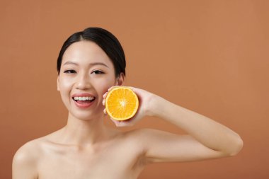 Kusursuz derisi olan, turuncunun yarısını tutan mutlu genç kadın.
