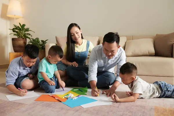 笑顔の両親と3人の息子が一緒に床に絵を描いている — ストック写真