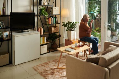 Düşünceli kıdemli bir adam arkadaş ya da aile üyesi için sesli mesaj kaydederken dışarıya bakıyor