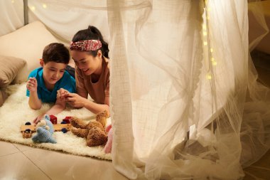 Gülümseyen anne ve oğul, çocuk odasına kurulmuş büyük bir çadırda yerde yatıyorlar.