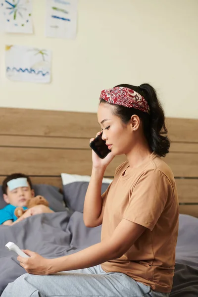 stock image Worried mother calling doctor after measuring body temperature of sick child with contactless thermometer