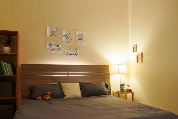 ベッドサイドテーブルにナイトランプとベッドの上に掛かる図面を持つ19歳の男の子の空の寝室 — ストック写真