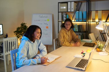 Üniversite yurdunun ortak odasında okuyan gülümseyen öğrenciler