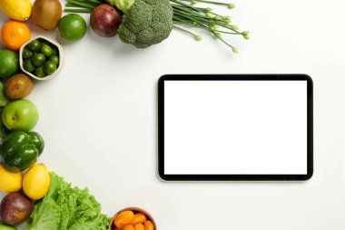 Dijital tablet beyaz masada, taze meyve ve sebze yığınının yanında.