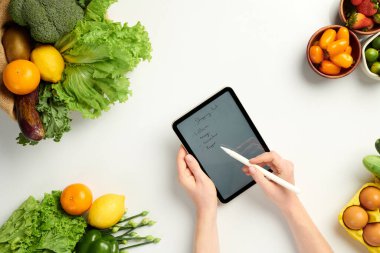 Dijital tablete alışveriş listesi yazan kişinin elleri