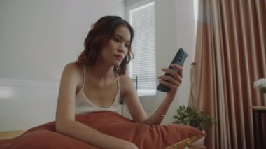 Genç, yorgun, esneyen bir kadının, uyumadan önce ya da sonra yatakta otururken akıllı telefona yapıştığı el kamerası görüntüsü.