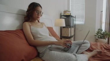 Kablosuz bilgisayarla çalışan, rahat bir odada oturan düşünceli bir kız öğrencinin ya da serbest çalışan bir çalışanın el kamerası görüntüsü.