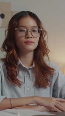 Genç kız öğrencinin ev ödevlerini yazarken ve kameraya bakarken çekilmiş dikey bir portre resmi.