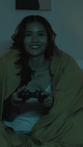 年轻女子晚上在床上玩电玩时玩乐的垂直镜头 — 图库视频影像