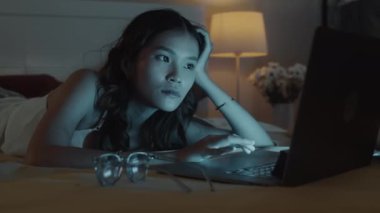 Gecenin bir yarısı dizüstü bilgisayarın önünde arkadaşlarıyla sohbet eden neşeli genç bir kadının orta boy fotoğrafı.