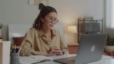 Genç Asyalı bir kadının video görüşmesi sırasında evdeki kablosuz bilgisayarı kullanarak iş arkadaşlarıyla konuştuğu orta boy bir fotoğraf.