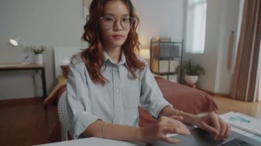 Genç yaşta ciddi bir kadın girişimcinin orta boy portresi masada oturuyor ve evde çalışırken dizüstü bilgisayarda yazıyor.