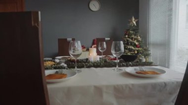 Şarap kadehleri, çatal bıçaklar, tabaklar ve aperatiflerle donatılmış bir şenlik masası. Arka planda yeni yıl ağacı, Noel kutlaması konsepti.