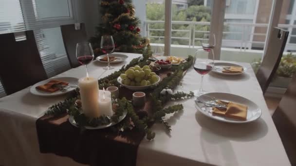 クリスマスのお祝いのために装飾された居心地の良いリビングルームの中長いショット 異なる前菜 ワインと燃えるろうそく バックグラウンドの新年の木 — ストック動画