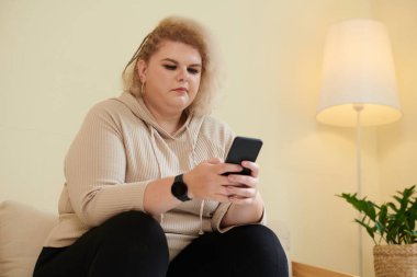 Artı, modern saç stili olan sarışın bir kadın arkadaşlarına mesaj atıyor veya akıllı telefondan sosyal medyayı kontrol ediyor.