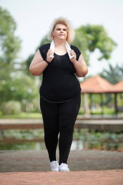 Şehir parkında antrenman yaptıktan sonra eve yürürken yorgun ve kilolu bir sporcu kadın.