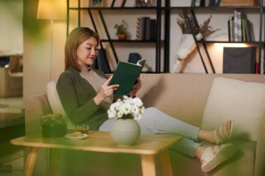 İyi bir kitap ve bir fincan çayla kanepede dinlenen pozitif bir genç kadın.