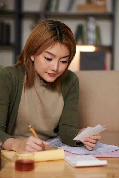 Young woman checking utility bills and receipts, managing monthly expenses and taking notes in planner