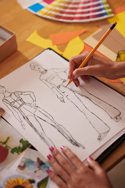 Hands of designer drawing fashion illustration at her desk