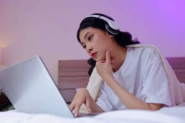 Young Asian blogger in headphones editing video on laptop, adding music and sound effects